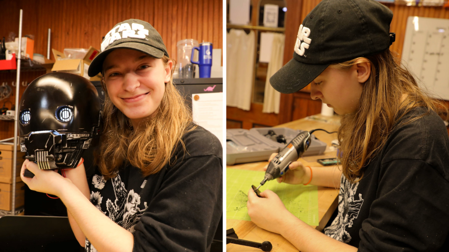 Brianna Bailey holds up her K-2SO helmet, and she holds a Dremel inside at her workspace.