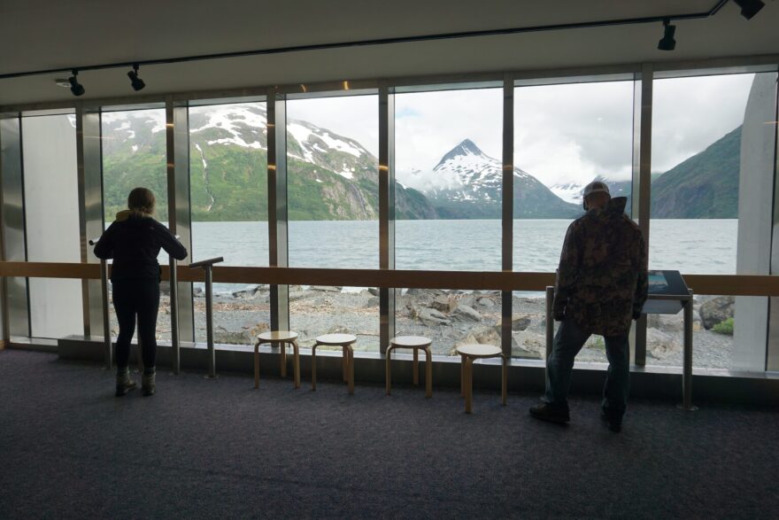 two people look out the window, at a lake and glaciers and mountains