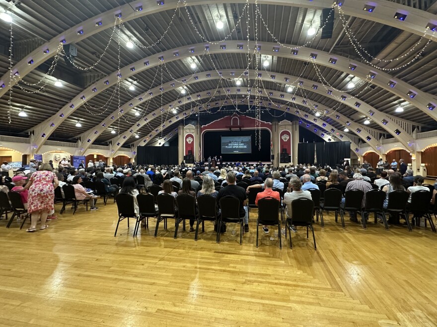 Crowd sits in chairs facing a stage in a classical styled auditorium.