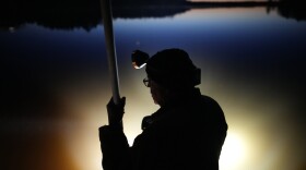 Lights illuminate the water as Mick Tainter holds a spear while fishing at the Chippewa Flowage on the Lac Courte Oreilles Reservation, Sunday, April 14, 2024, near Hayward, Wis. (AP Photo/John Locher)