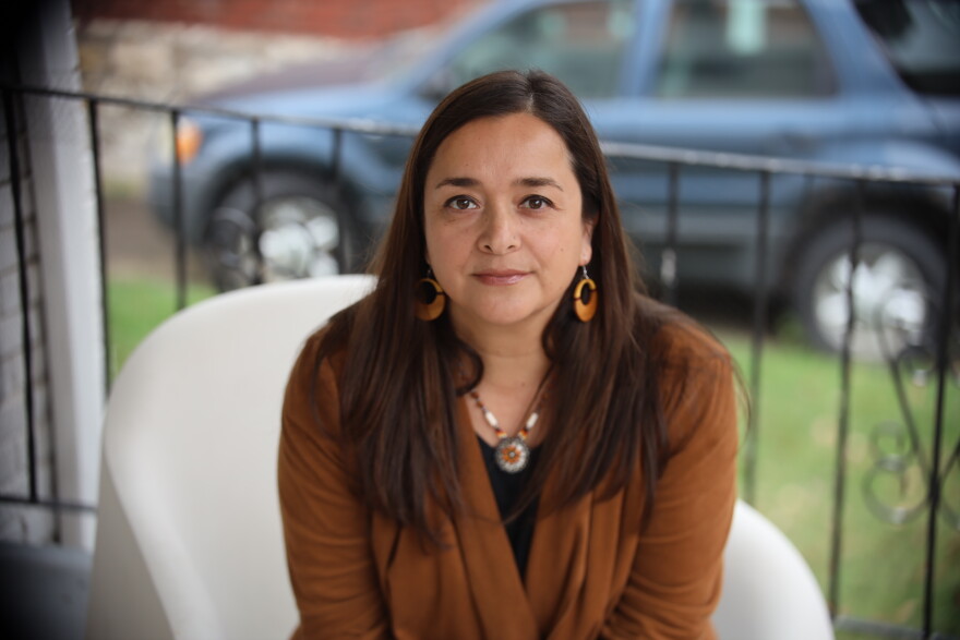 A woman poses for a photo sitting on a a white chair outside on a porch