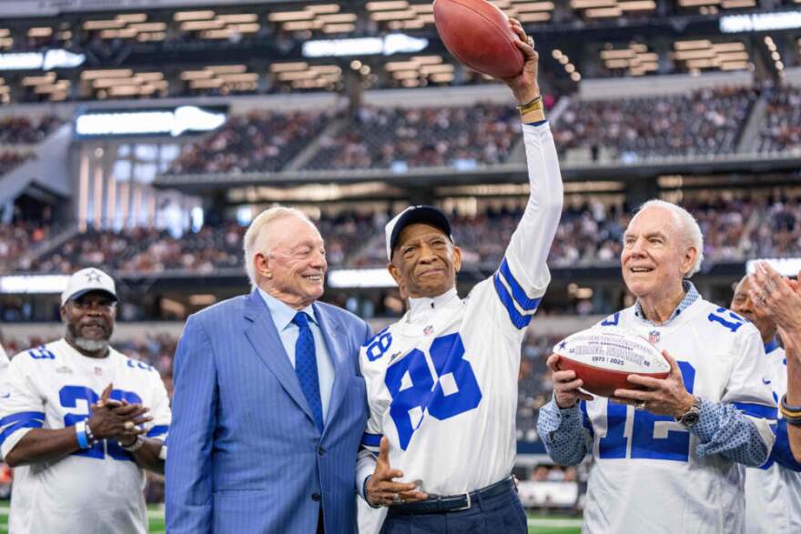 Dallas Cowboys owner Jerry Jones present commemorative footballs to former receiver Drew Pearson, center, and quarterback Roger Staubach, right, in honor of the 50th anniversary of their "Hail Mary" pass before a football game between the Cowboys and the Washington Commanders, Sunday, Oct. 19, 2025, in Arlington, Texas. (Jeffrey McWhorter/AP)