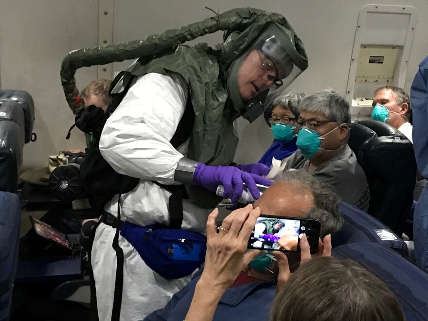 Checking for signs of COVID-19, a medical worker in a protective suit checks the temperatures of people who were on board the Diamond Princess cruise ship as they fly on a chartered evacuation plane from Japan to Lackland Air Force Base in Texas.