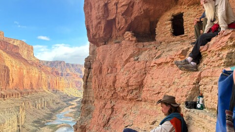 Two people sit along the wall of the Grand Canyon.