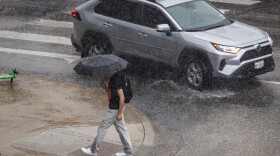 Photo of a man with an umbrella passing a car on a water-logged street