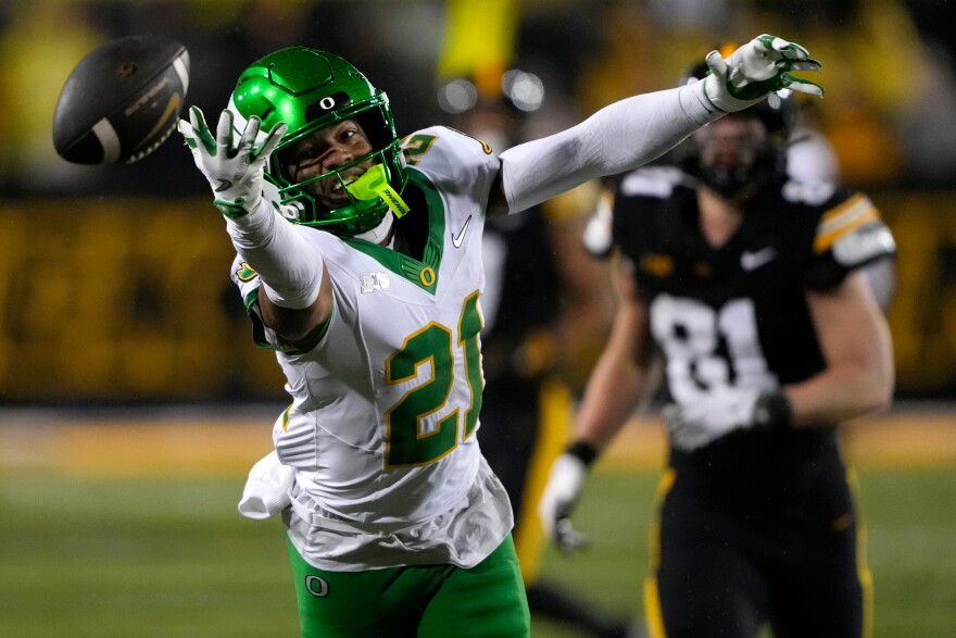 An Oregon football player reaches for a football that is just out of his reach