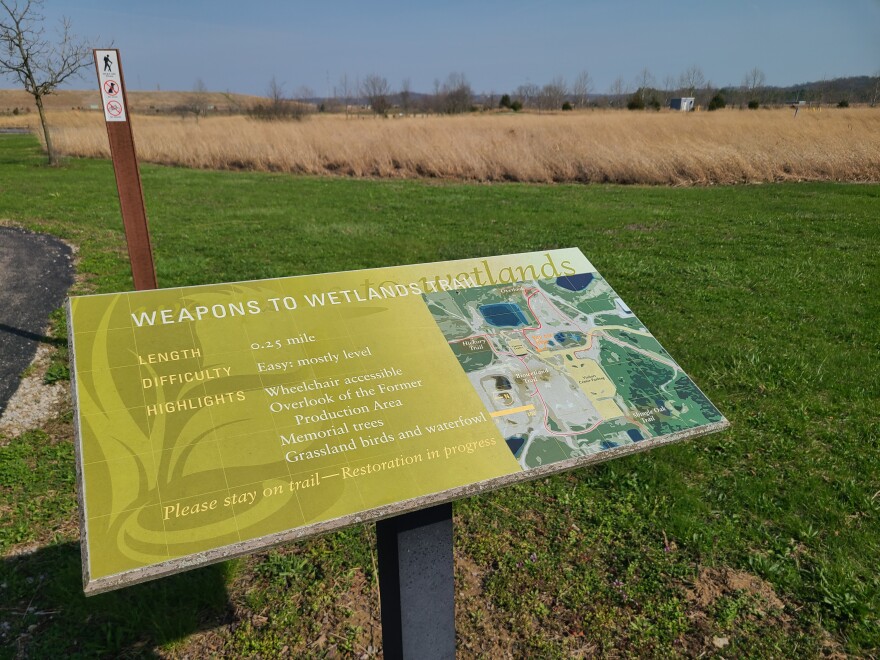 sign reading "weapons to wetlands trail" tall grasses and a hill are visible in the background
