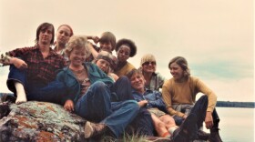 A group of young adults sits on a rock in front of a lake in 1976.