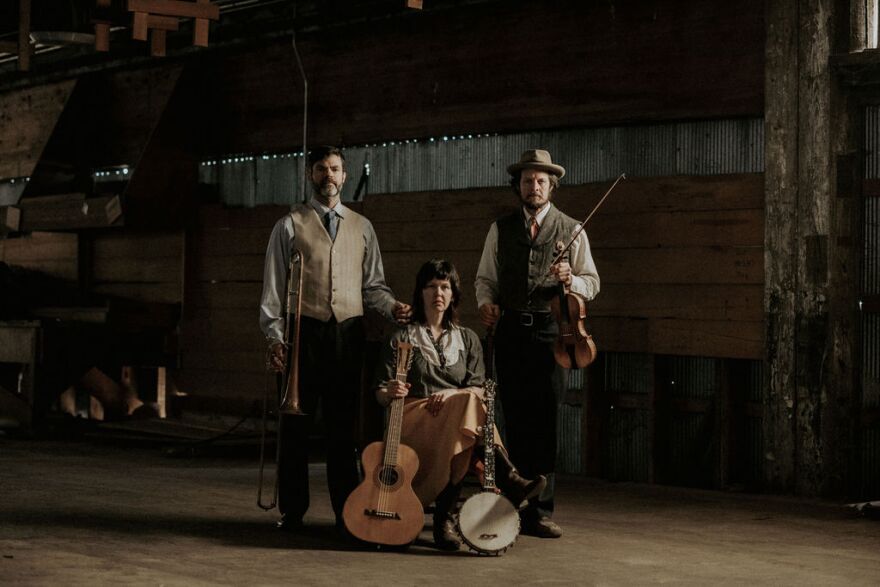 Three people posing with instruments. They are dressed in a vintage 1920s look.