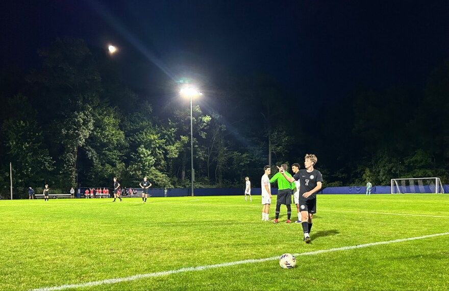 Center referee discusses a foul call with two East Lansing High School players while a DeWitt High School player retrieves the ball.