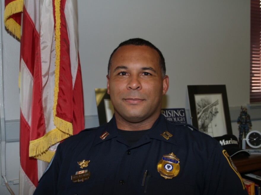 A uniformed officer stands in front of the American flag