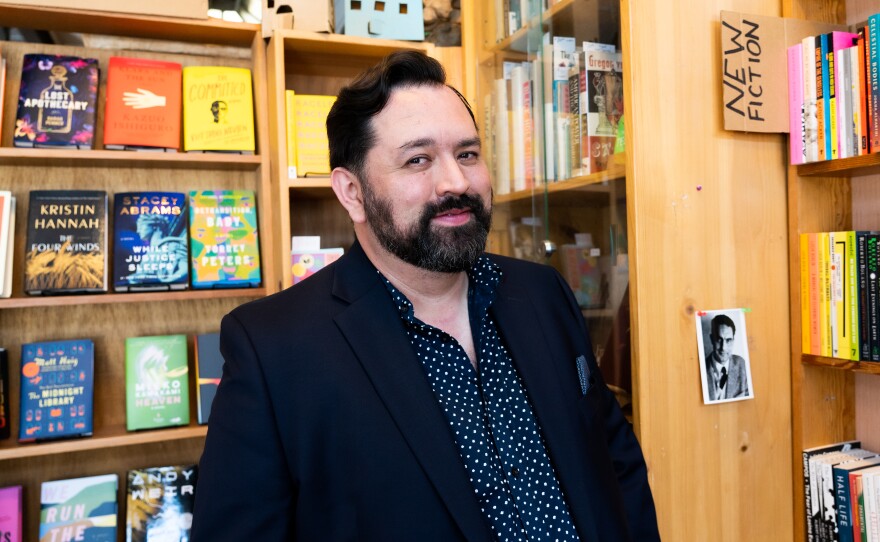 Latinx writer, organizer, and comedian Baruch Porras-Hernandez in front of books