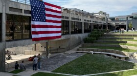 People gaze down at the site where Charlie Kirk was shot, above which hangs an American flag, at Utah Valley University, Monday, Sept. 15, 2025, in Orem, Utah.