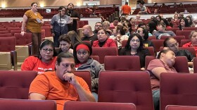 People in t-shirts and jeans sit in burgundy auditorium seats and listen intently as a woman asks a question at a microphone.