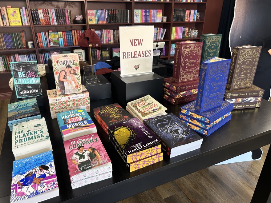 A black table with numerous romance novels on top of it with pink, blue, black, and white covers.