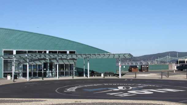 An airport terminal building overlooks a bay with a cantilever bridge in the background and a painted parking lot in the foreground with "Fly OTH" pained on it.