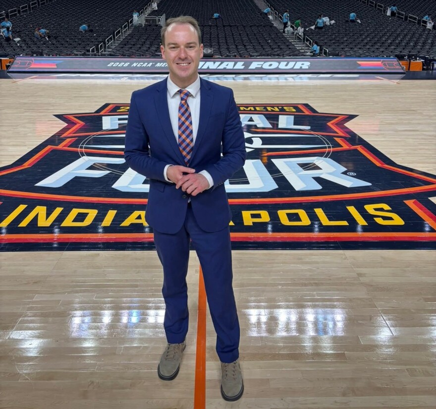 Man in a blue suit standing at center court in a large basketball arena with a Final Four logo inscribed on the court