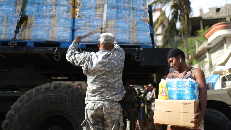 A U.S. Army soldier unloads a shipment of water provided by FEMA as a resident walks past in San Isidro, Puerto Rico.