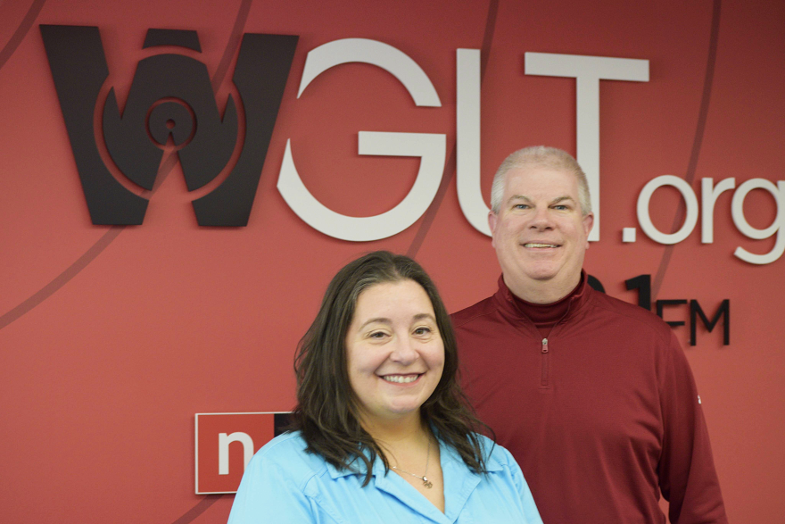 Woman in blue and man in red smile in front of WGLT logo.
