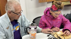 A man wearing a blue button up helping someone in a pink coat woodburn
