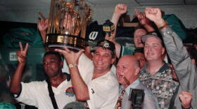 Don Smiley hoists the championship trophy in the Marlins locker room after the Marlins defeated the Cleveland Indians in Game 7 of the 1997 World Series. To his right with a cigar in his mouth is club owner H. Wayne Huizenga.