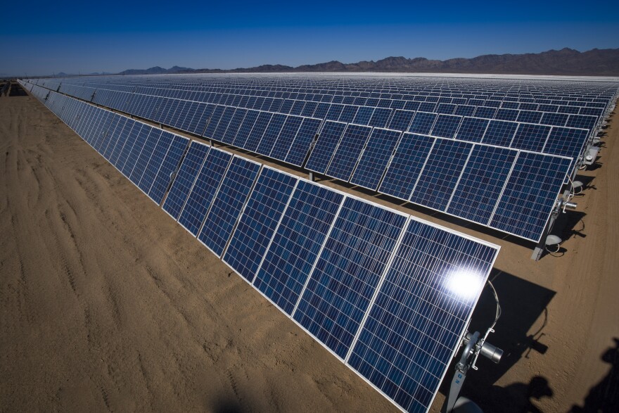 A desert with several rows of solar panels stretching from the foreground to the background.