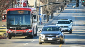 A red commuter bus rides in the left lane of a street with other car traffic moving alongside of it.