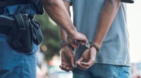 a police office handcuffs a man, the man has his hands cuffed behind his back