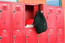A black backpack hanging on the door to red lockers with books inside.
