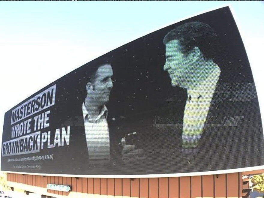 A Wichita billboard tying Masterson to former Kansas Gov. Sam Brownback, a common attack for Holscher, as both candidates attempt to appeal to moderate voters.