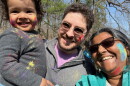 A man and woman pose with a child. All three have paint splattered on parts of their face.