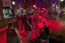 People walk through a narrow park, bathed in red light.