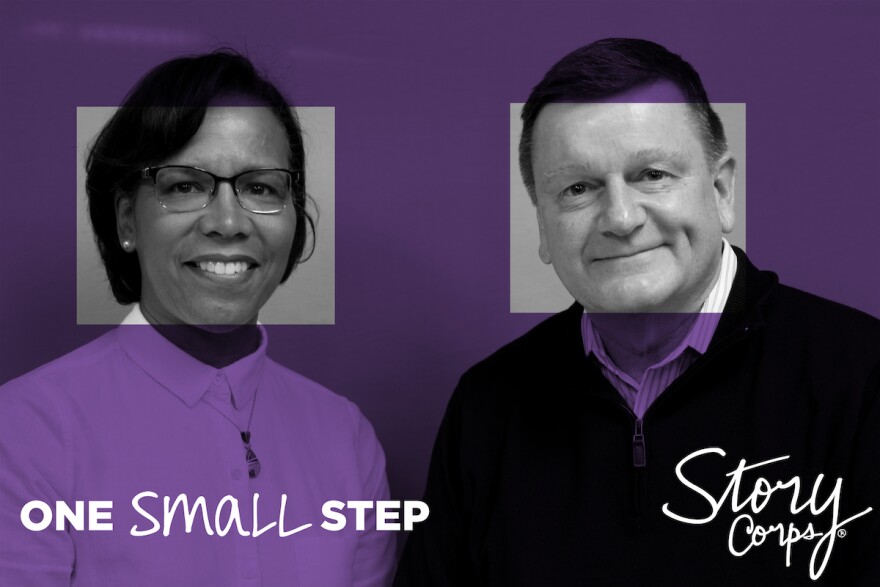 A woman and man who met at a One Small Step conversation are standing next to each other while looking toward the camera and smiling. The StoryCorps and One Small Step logos are layered on top of the photo.