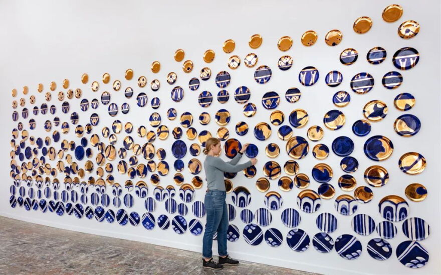 Ceramic artist Molly Hatch adjusts one of the 450 earthenware plates that comprise her 'Amalgam' exhibition.