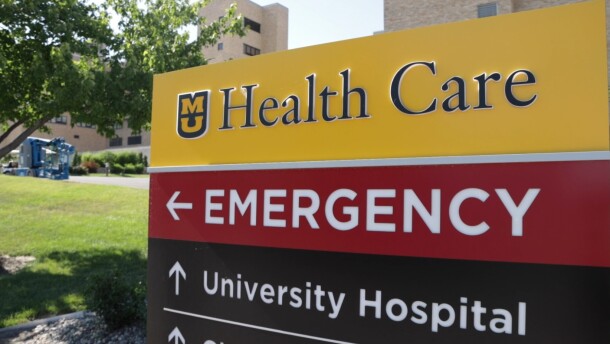 A image of the MU Healthcare sign. The top part is yellow and reads "MU Healthcare" the middle part is red and says "Emergency" with an arrow, the bottom part is black and reads "University Hospital" with an arrow. 