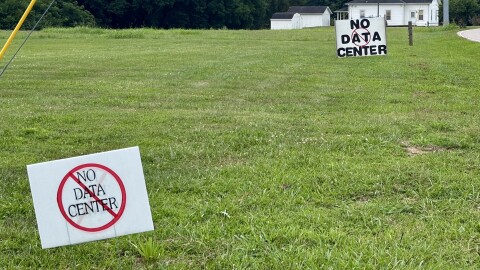 In a field of grass, two signs, one larger than the other, depict the words "No data center" with a prohibition symbol.
