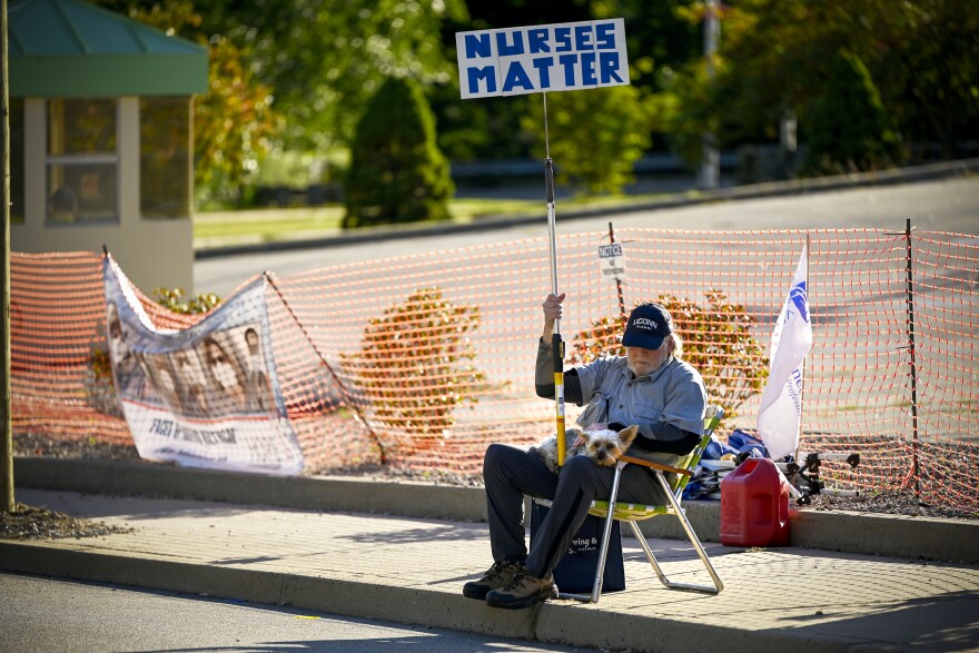 A man sitting in a folding chair with his dog outside Windham Community Memorial Hospital holding a sign that reads "Nurses Matter" in support of the Windham Hospital Nurses Strike.