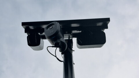A Flock camera with a solar panel sits on a pole.