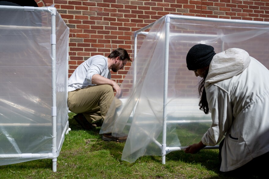 Two people attach plastic sheeting to cubes made out of PVC pipe.