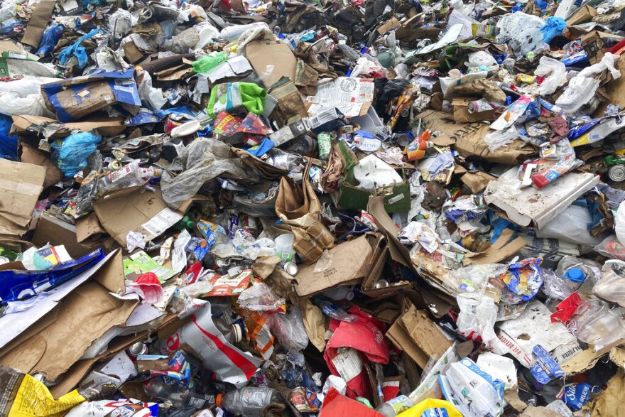 A mass of recycled materials, mostly cardboard and plastic, lie in a pile at a recycling facility.
