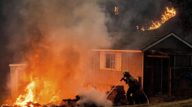 FILE - In this Dec. 3, 2020 file photo a firefighter works to keep flames from a structure while battling the Bond Fire burning in Orange County, Calif. As consecutive years of catastrophic wildfires drive up the cost of insuring homes across California, state regulators announced on Monday, Feb. 8, 2021, a step toward creating incentives for retrofitting older homes to make them more resilient to fires. (AP Photo/Noah Berger, File)