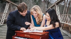 Neave Trio, standing on old bridge, pouring over a musical score while leaning on a small piano