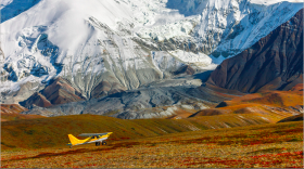 A single prop plane sits in front of large snowcapped mountains in the distance. 