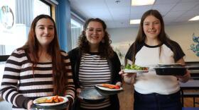 Three high school seniors smile, holding their lunches