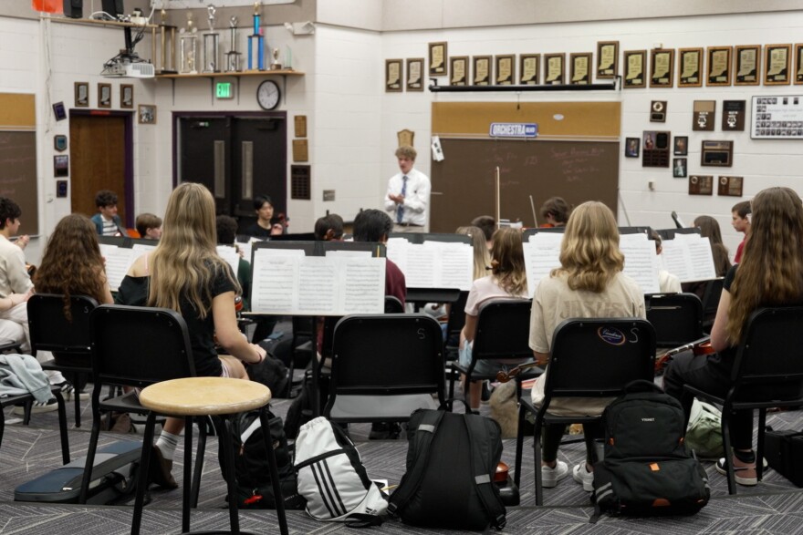 The Hoosier Youth Philharmonic Orchestra is made up of musicians from Bloomington High School North and South. Students sit in front of music stands with sheet music with their instruments. 