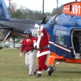 Santa Claus and a helper disembark from a helicopter during Operation Santa Delivery.