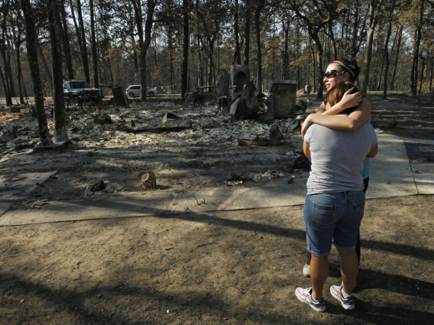 The remains of their burned home in the background, Gaye Jaco (front) hugged her stepdaughter Jennifer Leaver on Tuesday in Bastrop, Texas.