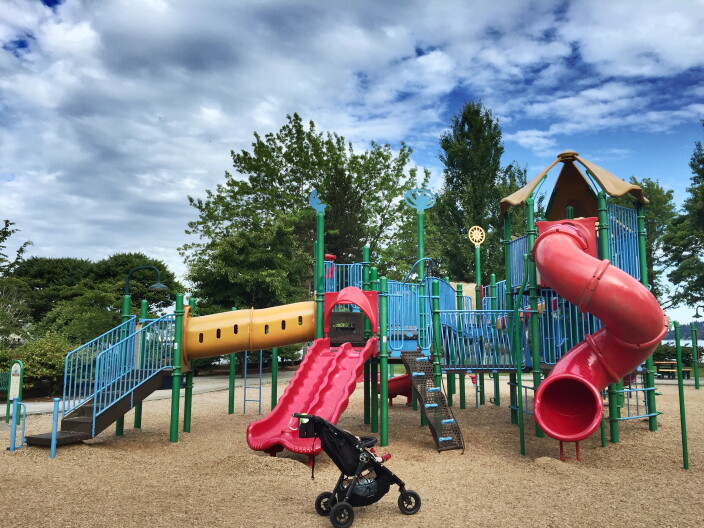A stroller sits in front of a large playground set.