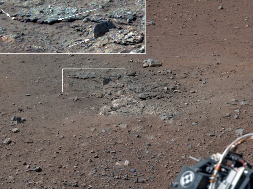 With the loose debris blasted away by the rockets, details of the underlying materials are clearly seen. Shown in the inset in the figure are pebbles up to 1.25 inches across (upper two arrows) and a larger clast 4 inches long protruding up by about 2 inches from the layer in which it is embedded.