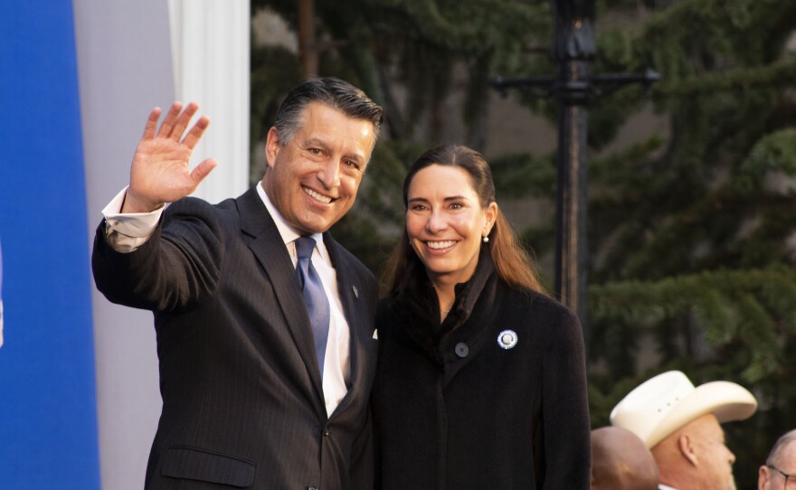 A man and woman smile for the camera. The man is waving. 